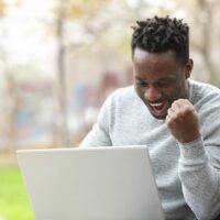 Excited black man checking laptop in a park